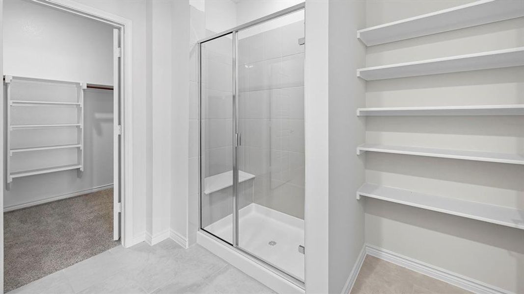 Full bath with a walk in closet, a stall shower, light carpet, and light tile patterned floors