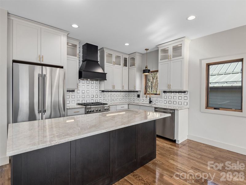 Designer kitchen featuring granite countertops, large center island, Thermador appliances, Wolf Home Products cabinetry, and striking tile backsplash.