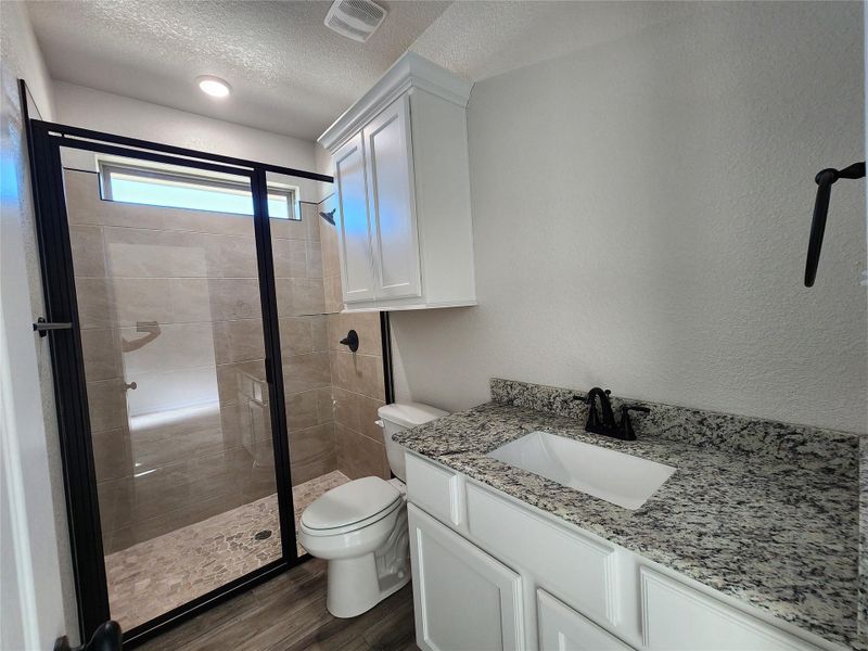 Bathroom featuring a shower stall, vanity, a textured ceiling, a textured wall, and dark wood-style floors