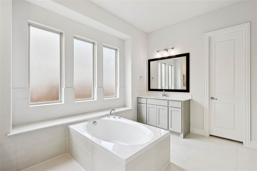 Bathroom featuring tile patterned flooring, tiled bath, and vanity