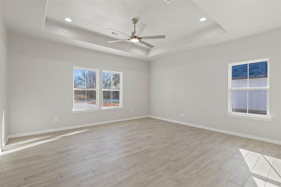 Empty room featuring ceiling fan, a tray ceiling, and light hardwood / wood-style flooring Empty room featuring ceiling fan, a tray ceiling, and light hardwood / wood-style flooring