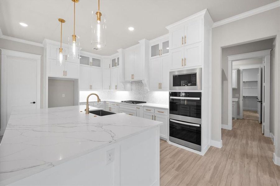 Kitchen with light stone countertops, stainless steel appliances, sink, decorative light fixtures, and white cabinets