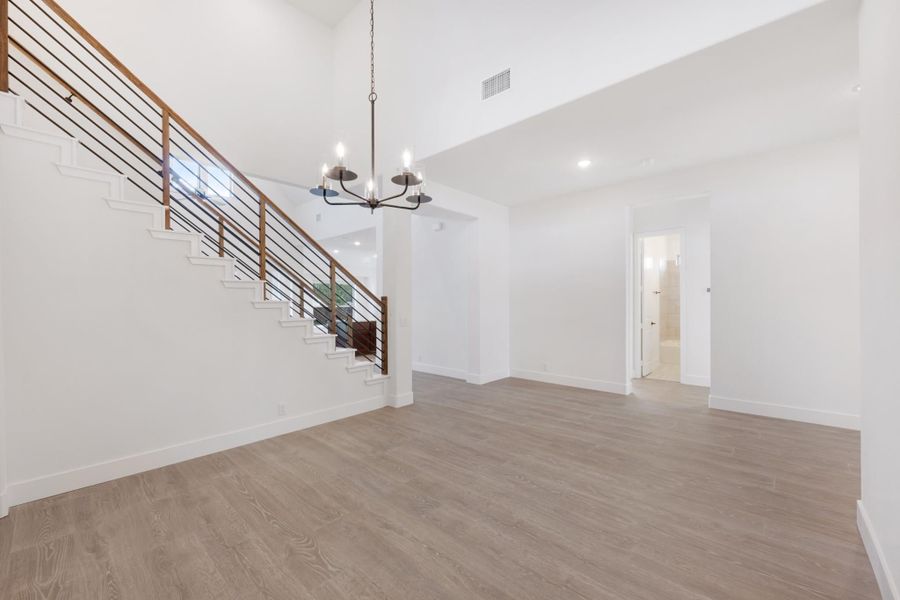 Open living area with high ceilings, wood-railed staircase, chandelier, and light hardwood floors