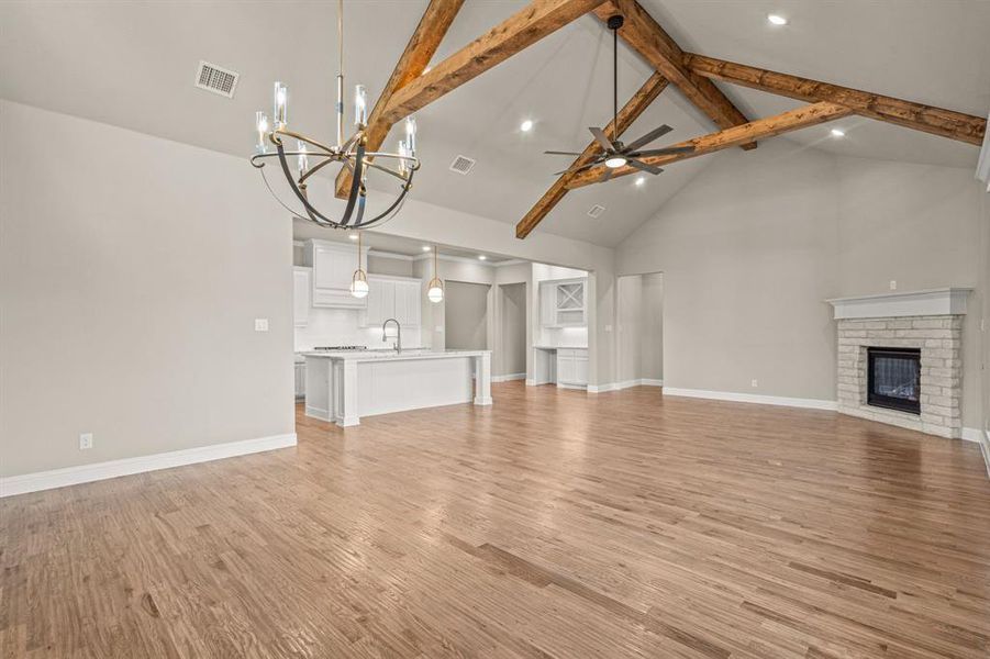 Unfurnished living room with high vaulted ceiling, a fireplace, ceiling fan, light wood-style floors, and a chandelier
