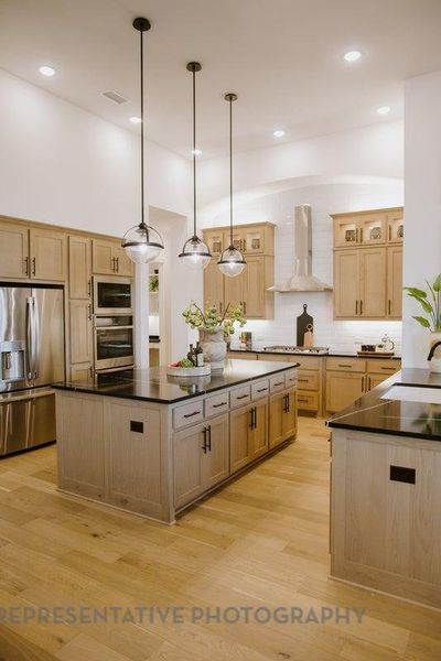 Kitchen with stainless steel appliances, wall chimney range hood, dark countertops, a kitchen island, and lofted ceiling Kitchen with stainless steel appliances, wall chimney range hood, dark countertops, a kitchen island, and lofted ceiling