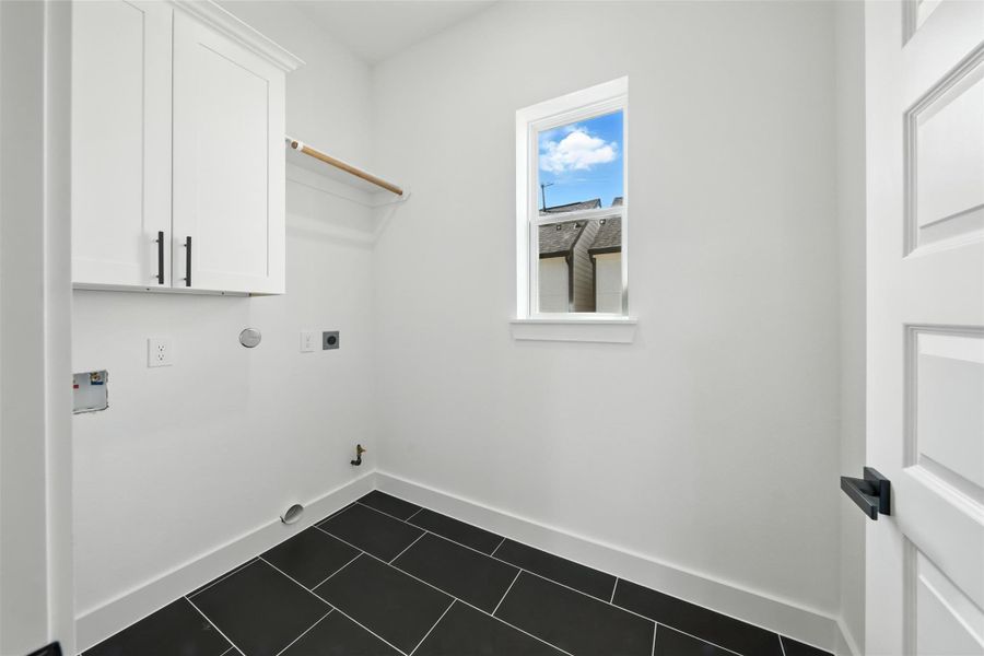 Functional laundry room with clean finishes, featuring upper cabinetry for storage, utility connections, and a window for natural light. Sleek tile flooring adds durability while keeping the space bright and practical. Functional laundry room with clean finishes, featuring upper cabinetry for storage, utility connections, and a window for natural light. Sleek tile flooring adds durability while keeping the space bright and practical.