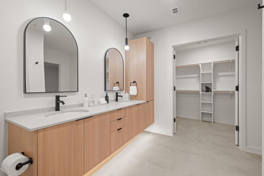The primary bath in the Shady Grove palette features warm cabinetry, black hardware, quartz countertops, and a glass enclosed shower for a clean, modern look.