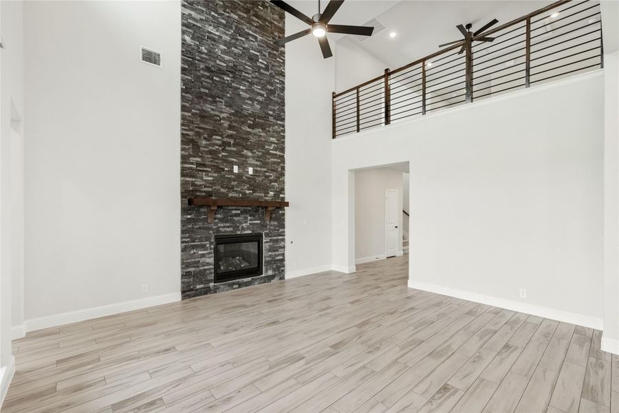 Open living room with two-story ceiling, floor-to-ceiling stone fireplace, wood floors, and upper loft railing