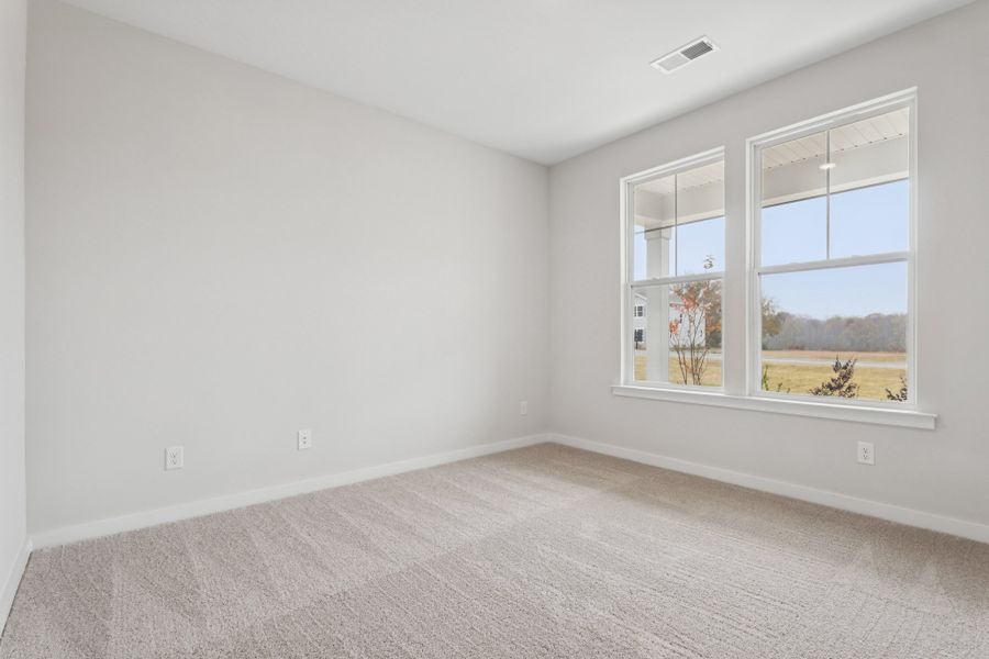 A room with a window and a white wall with a view of a field and trees.