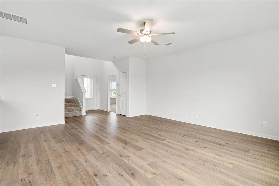 Unfurnished living room with stairs, light wood-style floors, and a ceiling fan