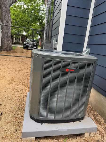 Trane HVAC unit on a level pad, set against the property's dark blue horizontal siding