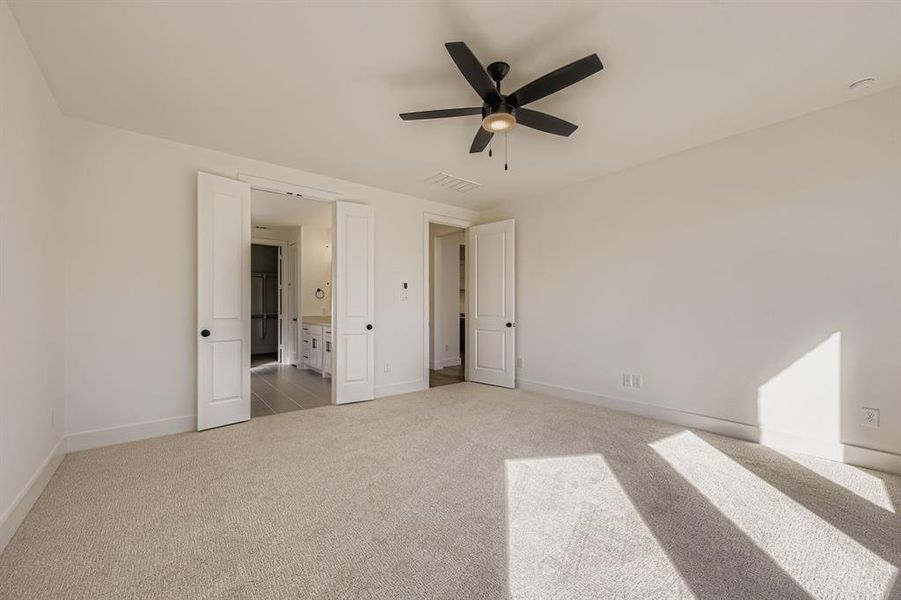 Unfurnished bedroom with light colored carpet, a ceiling fan, and connected bathroom