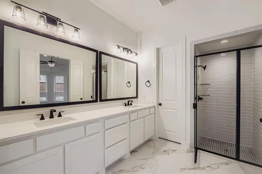 Full bath featuring a shower stall, double vanity, light marble finish floors, and ceiling fan