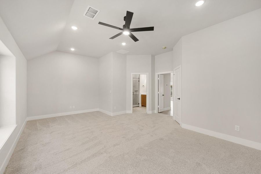 Empty bedroom with vaulted ceiling, black ceiling fan, carpet flooring, and open doors to ensuite bathroom and closet. Empty bedroom with vaulted ceiling, black ceiling fan, carpet flooring, and open doors to ensuite bathroom and closet.