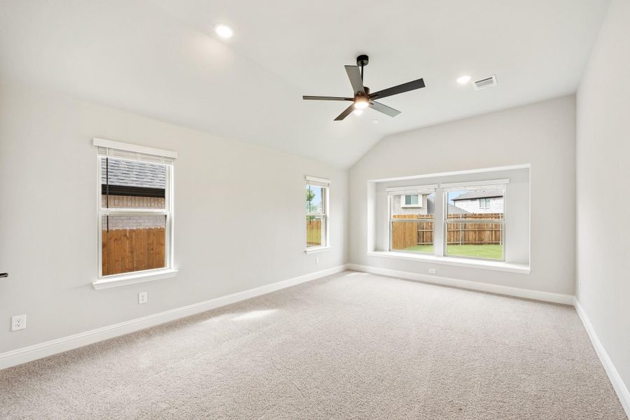 Empty bedroom with vaulted ceiling, ceiling fan, carpet flooring, and multiple windows overlooking backyard Empty bedroom with vaulted ceiling, ceiling fan, carpet flooring, and multiple windows overlooking backyard