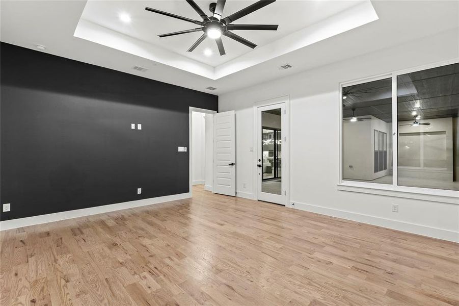 Empty room with light wood-type flooring, ceiling fan, visible vents, and a raised ceiling