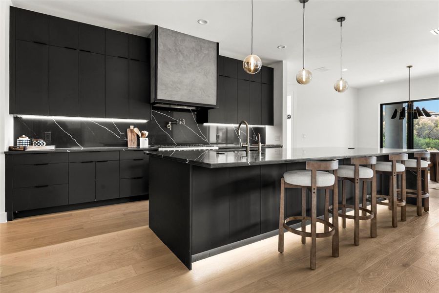 Kitchen featuring dark cabinetry, modern cabinets, a large island, pendant lighting, and light wood-style flooring Kitchen featuring dark cabinetry, modern cabinets, a large island, pendant lighting, and light wood-style flooring