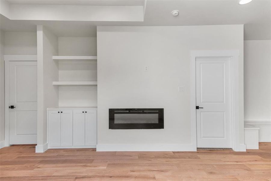 Integrated linear fireplace with a built-in shelving unit and lower cabinetry, complemented by wood-finish flooring