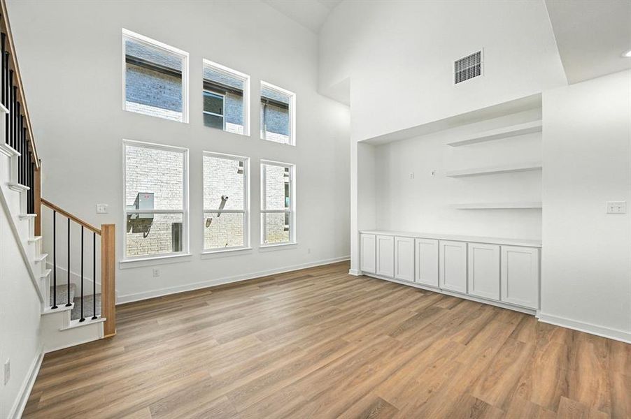 Unfurnished living room featuring light wood-style flooring, stairway, and a high ceiling