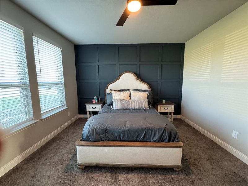 Carpeted bedroom featuring a decorative wall, ceiling fan, and an accent wall Carpeted bedroom featuring a decorative wall, ceiling fan, and an accent wall