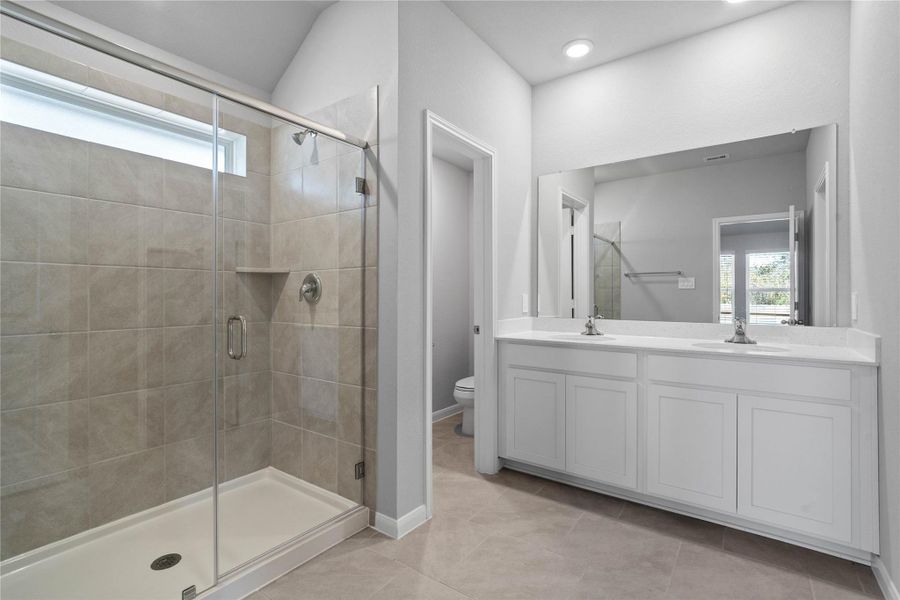 A bright and functional primary bath offering dual sinks for busy mornings, a large mirror, and a modern glass-enclosed shower, creating a serene and efficient space.