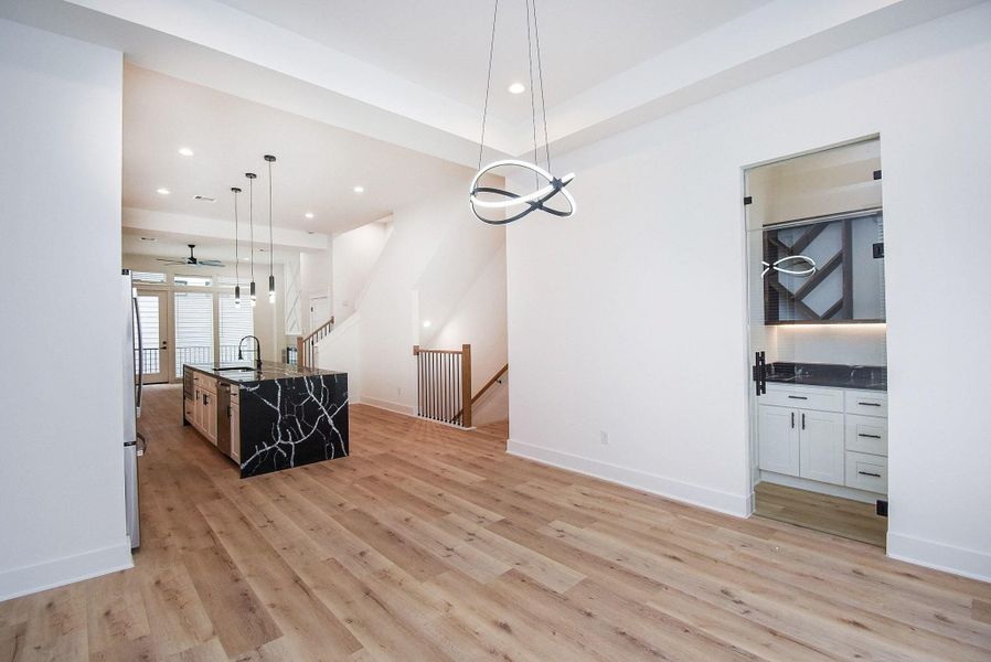 This modern open-concept space features sleek hardwood floors, a stylish black marble kitchen island, contemporary lighting, and ample natural light from large windows.