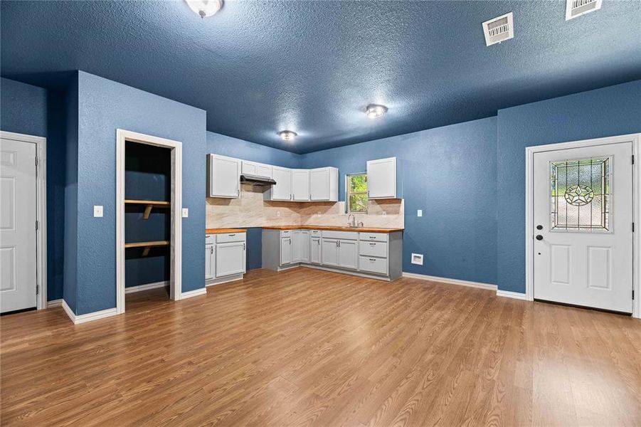 Kitchen with light hardwood / wood-style flooring, a textured ceiling, backsplash, sink, and white cabinetry Kitchen with light hardwood / wood-style flooring, a textured ceiling, backsplash, sink, and white cabinetry