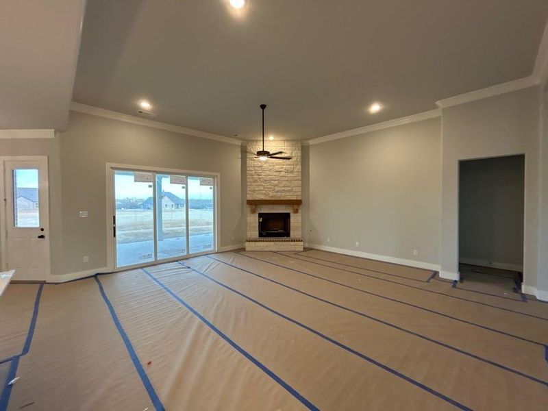 Unfurnished living room with a stone fireplace, ceiling fan, recessed lighting, and ornamental molding