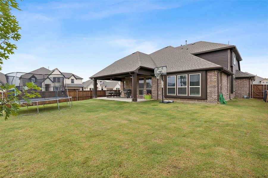 Rear view of house with a patio, a fenced backyard, brick siding, and a trampoline