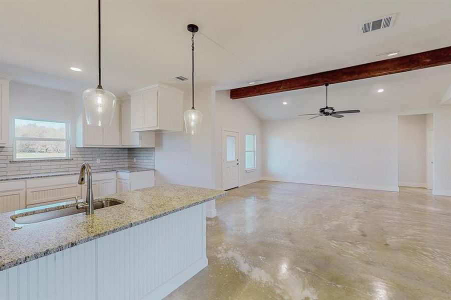 Kitchen with white cabinetry, sink, hanging light fixtures, tasteful backsplash, and lofted ceiling with beams