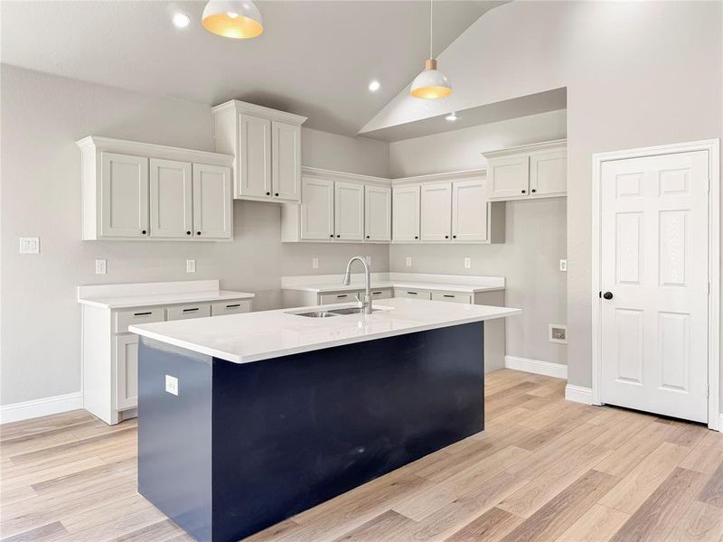 Kitchen featuring an island with sink, white cabinetry, lofted ceiling, light wood-style floors, and hanging light fixtures Kitchen featuring an island with sink, white cabinetry, lofted ceiling, light wood-style floors, and hanging light fixtures
