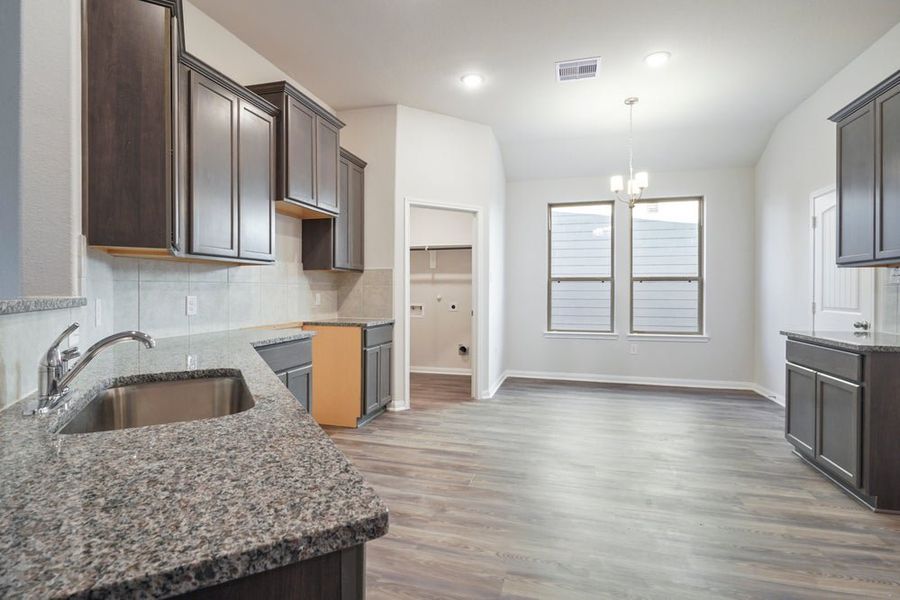 Open-concept kitchen and living area with dark gray cabinets, granite countertops, and wood-look flooring