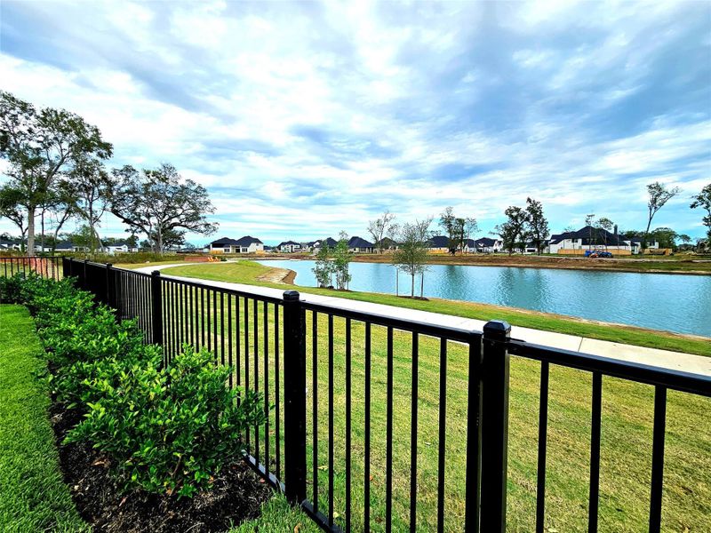This photo showcases a serene backyard view with a black metal fence, well-maintained landscaping, and a peaceful pond, offering a picturesque and relaxing environment in a residential neighborhood.