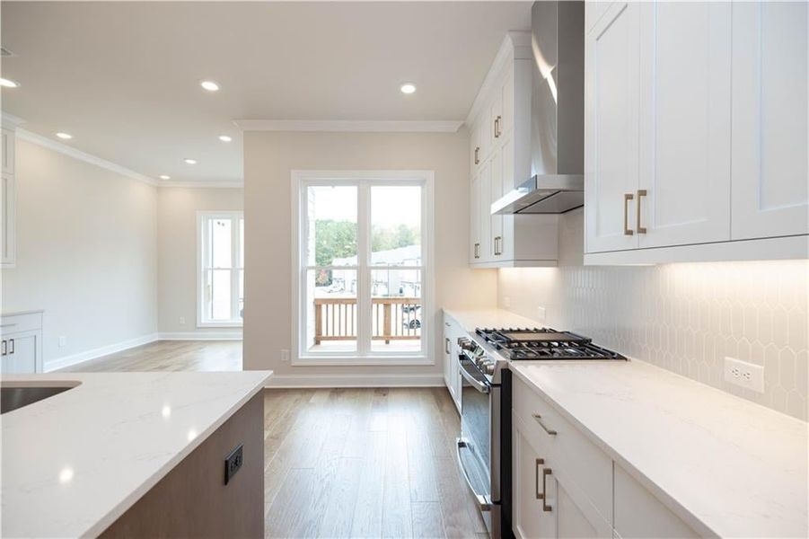 Kitchen with white cabinetry, wall chimney range hood, gas range, and light stone countertops