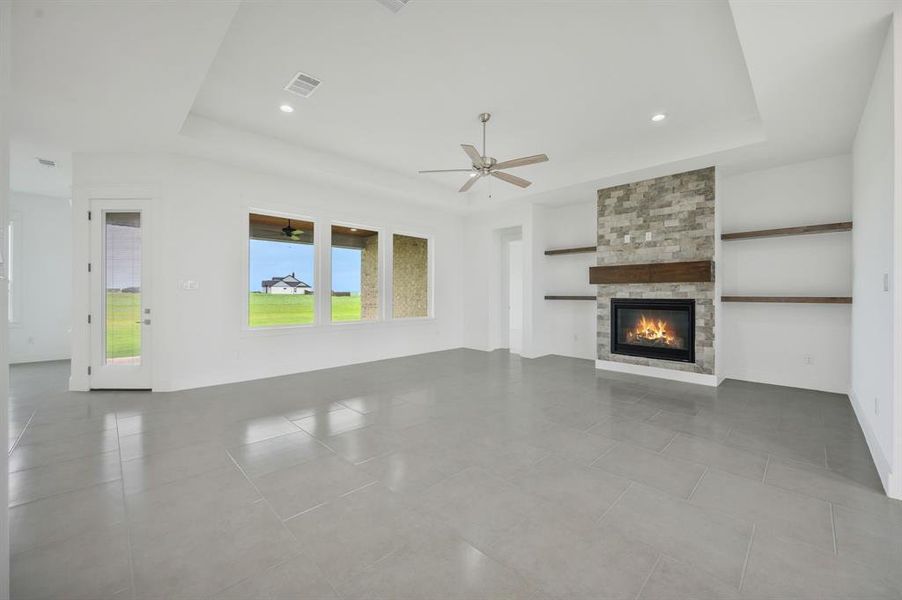 Unfurnished living room with visible vents, a ceiling fan, a raised ceiling, and a tile fireplace Unfurnished living room with visible vents, a ceiling fan, a raised ceiling, and a tile fireplace