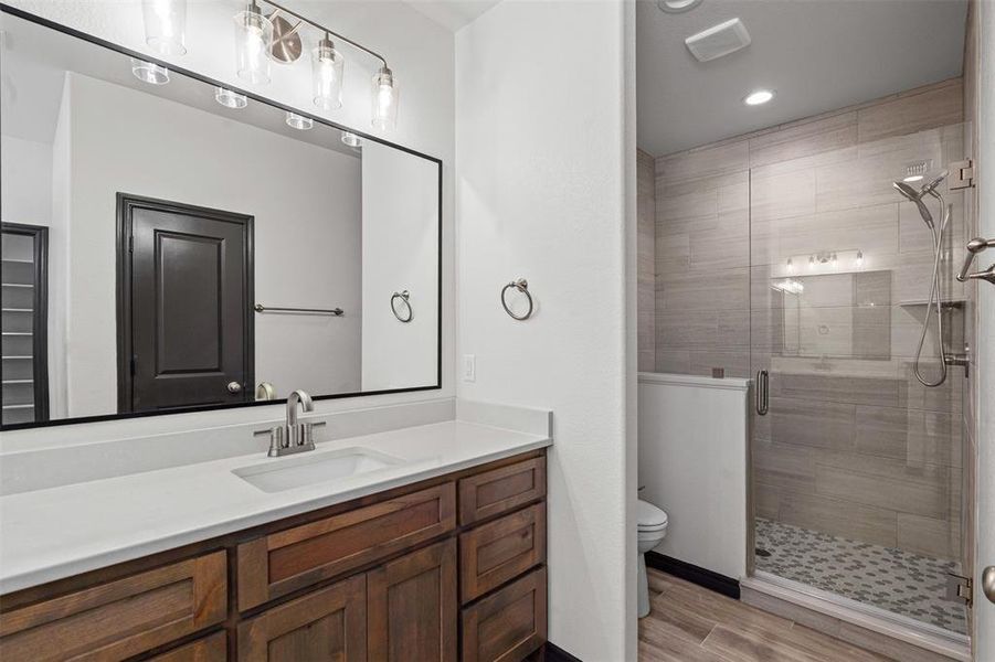 Bathroom with a stall shower, vanity, wood finished floors, and recessed lighting