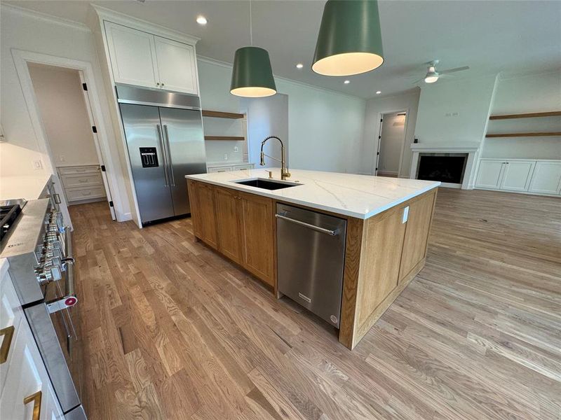 Kitchen with appliances with stainless steel finishes, light wood-type flooring, light stone countertops, an island with sink, and white cabinetry