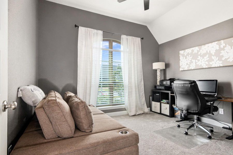 This cozy home office features a large window with sheer curtains, providing ample natural light and neutral decor, perfect for a productive work environment.