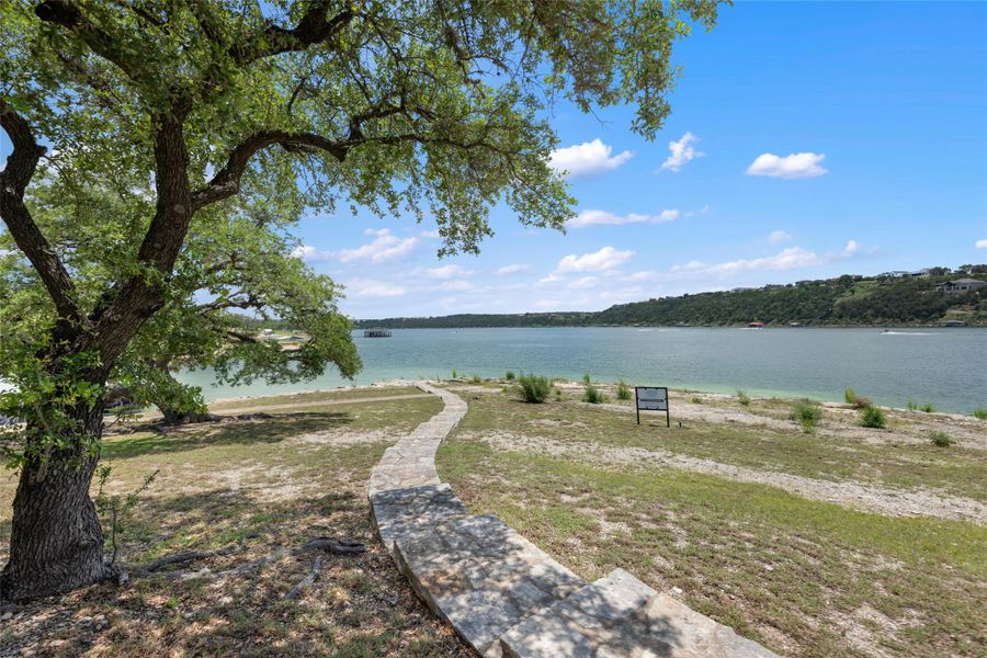 A stone pathway leads down to the tranquil lakefront, shaded by a mature tree, with distant hillside homes completing the picturesque scene. A stone pathway leads down to the tranquil lakefront, shaded by a mature tree, with distant hillside homes completing the picturesque scene.