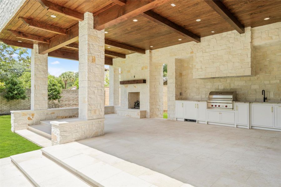 The expansive covered loggia is designed for outdoor living and entertaining, with a fully equipped summer kitchen, built-in Wolf grill, and fireplace. Limestone walls and flooring pair with a richly stained wood ceiling and exposed beams, creating a warm, beautifully finished extension of the home. The expansive covered loggia is designed for outdoor living and entertaining, with a fully equipped summer kitchen, built-in Wolf grill, and fireplace. Limestone walls and flooring pair with a richly stained wood ceiling and exposed beams, creating a warm, beautifully finished extension of the home.