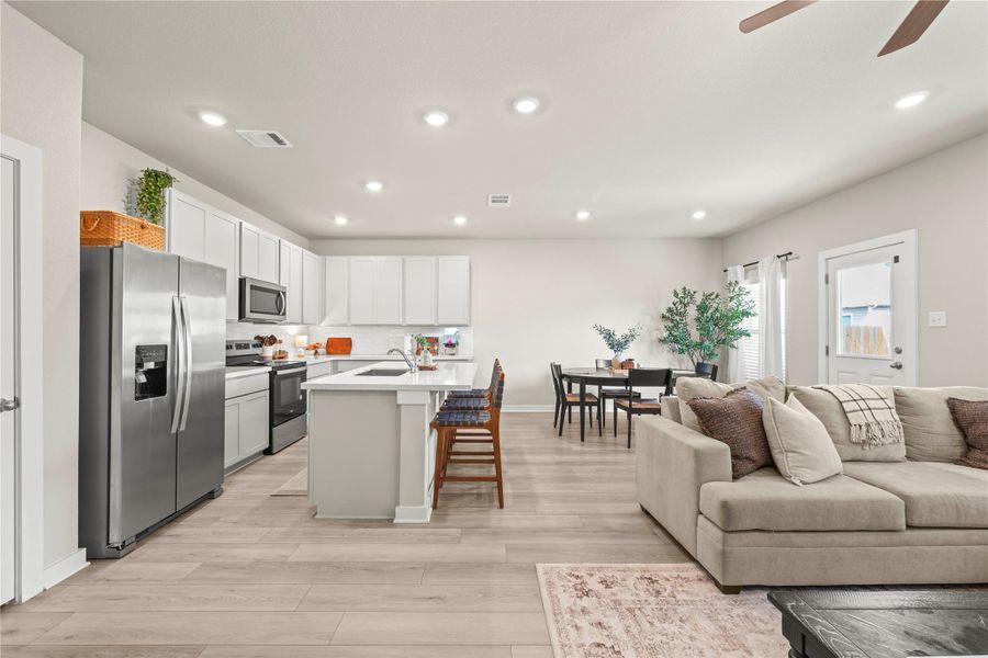 An open-concept living area with integrated kitchen, dining space, and comfortable seating, all illuminated by recessed lighting. An open-concept living area with integrated kitchen, dining space, and comfortable seating, all illuminated by recessed lighting.