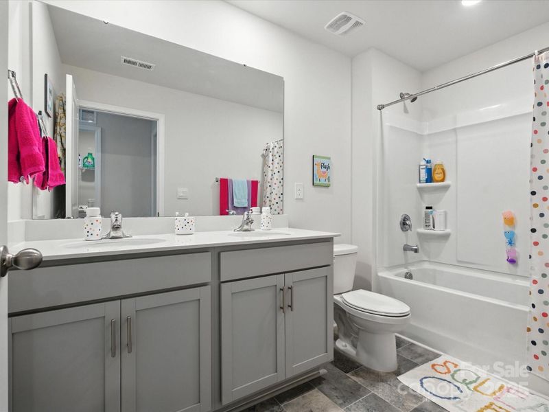Well-appointed full bathroom with dual vanity, granite countertops, and tub/shower combination. Gray cabinetry and tile flooring coordinate with home's modern aesthetic while providing family functionality.