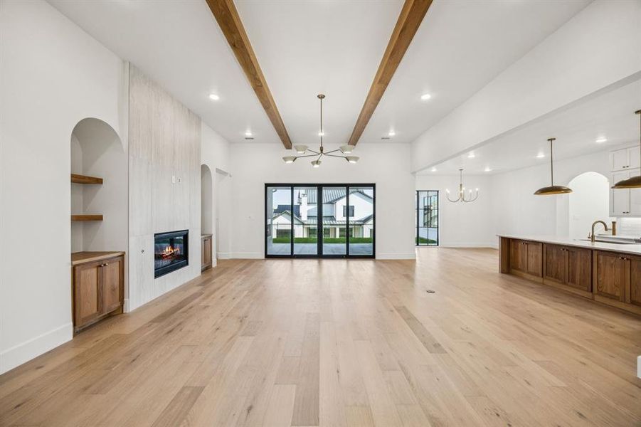 Unfurnished living room with a chandelier, a tiled fireplace, light wood-type flooring, beam ceiling, and recessed lighting Unfurnished living room with a chandelier, a tiled fireplace, light wood-type flooring, beam ceiling, and recessed lighting