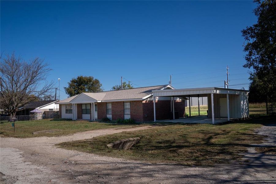 View of front of property featuring brick siding, dirt driveway, and an attached carport