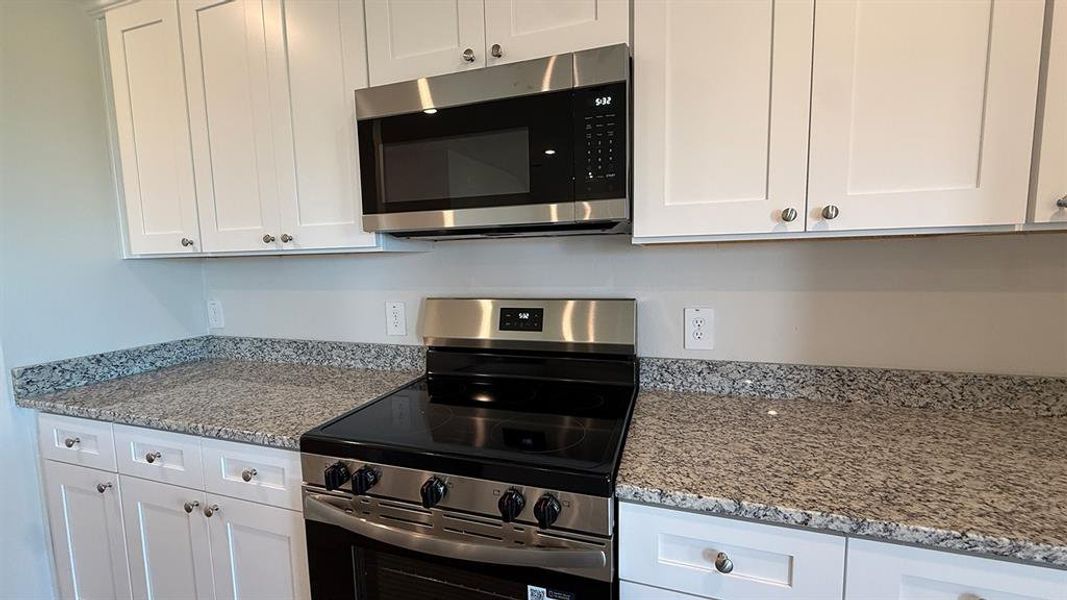 Kitchen featuring white shaker-style cabinetry, stainless steel appliances, and speckled countertops