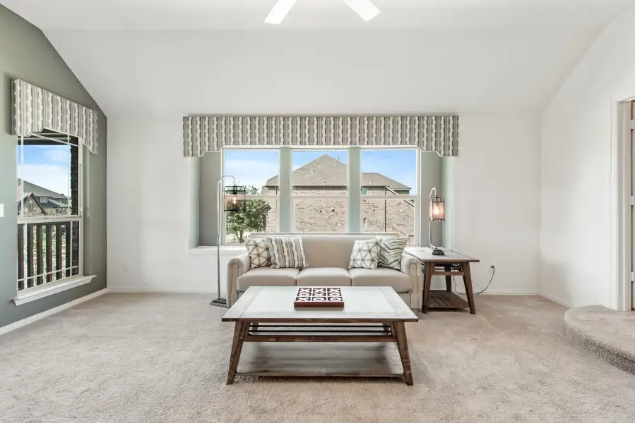 Living room with beige carpet, neutral sofa, wood coffee table, and large windows with valances