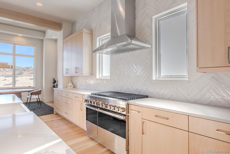 Light wood cabinetry pairs with a honed-stone perimeter and herringbone tile extending to the ceiling—an interplay of tone and texture that feels both serene and elevated.
