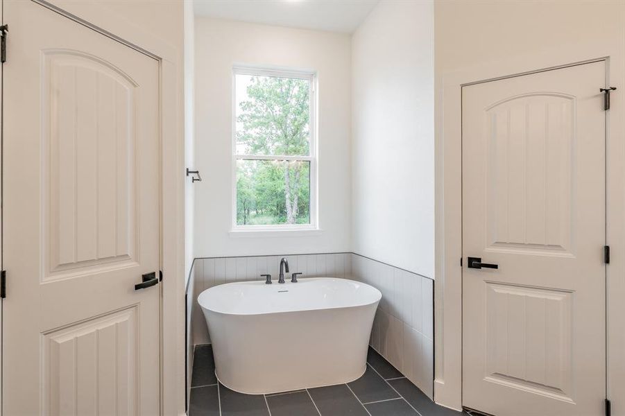 Full bath featuring a wainscoted wall, healthy amount of natural light, a freestanding bath, and tile patterned floors