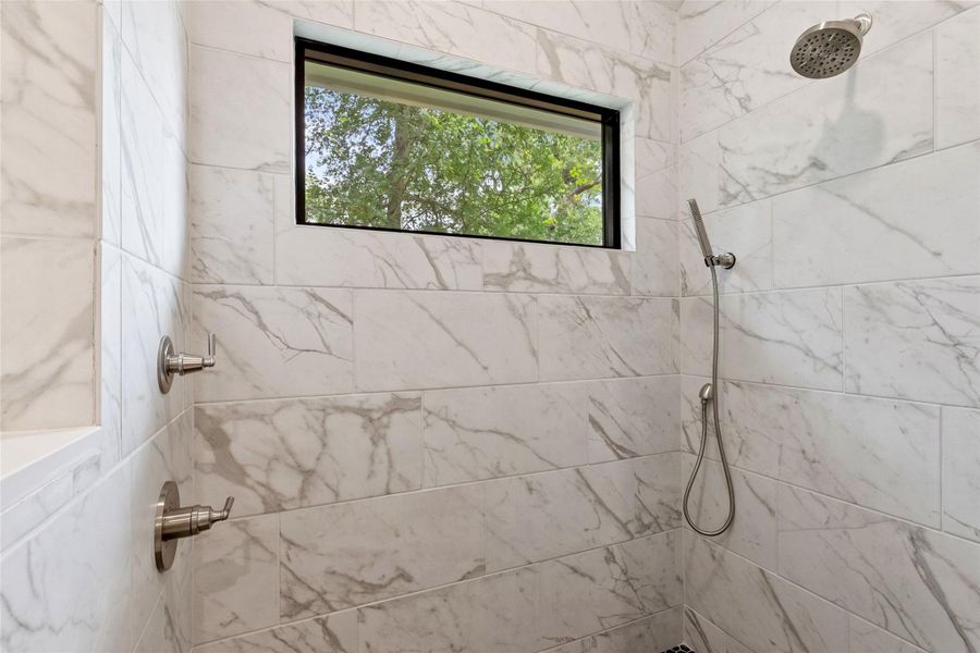 Marble-tiled shower with a rainfall shower head and a convenient handheld sprayer.