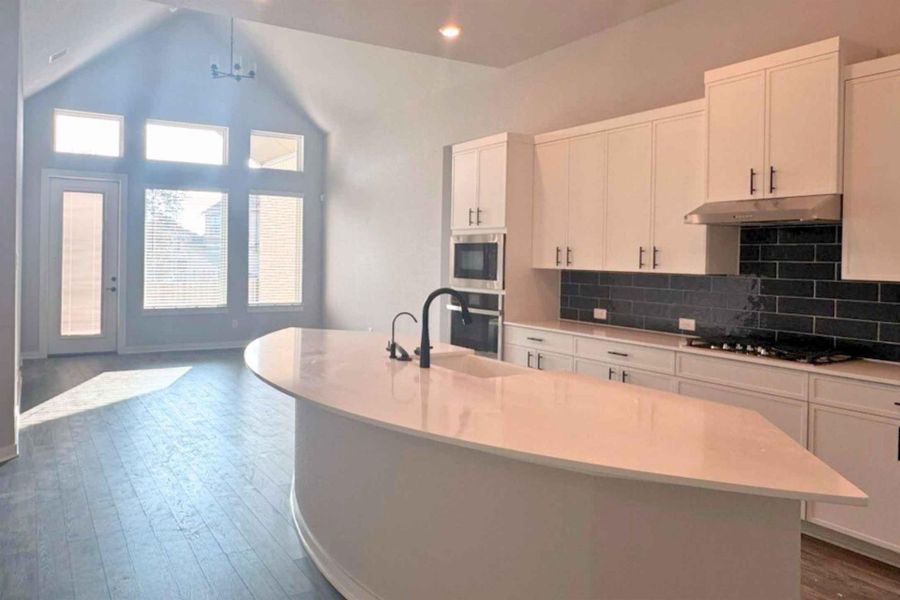 Kitchen with dark wood-type flooring, a center island with sink, white cabinets, stainless steel appliances, and high vaulted ceiling Kitchen with dark wood-type flooring, a center island with sink, white cabinets, stainless steel appliances, and high vaulted ceiling